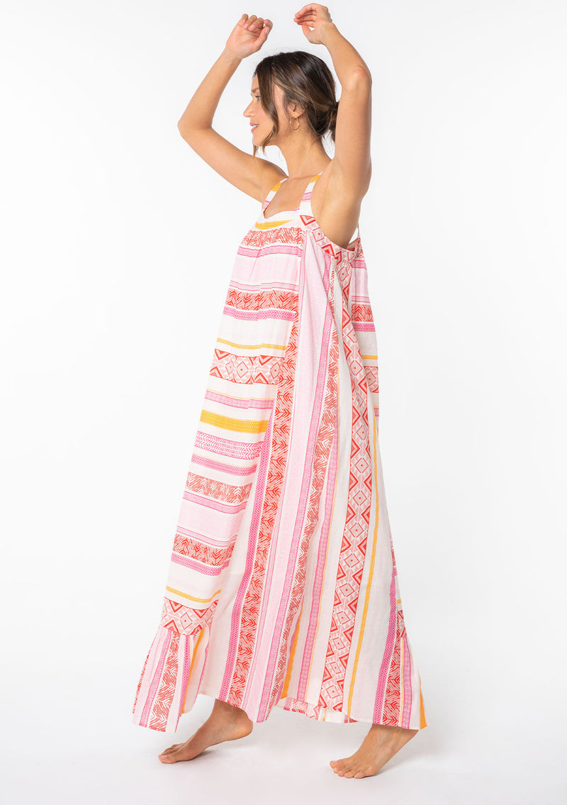 [Color: Fuchsia/Orange] A model wearing a flowy bohemian cotton beach maxi dress in a pink and white multi striped pattern.
