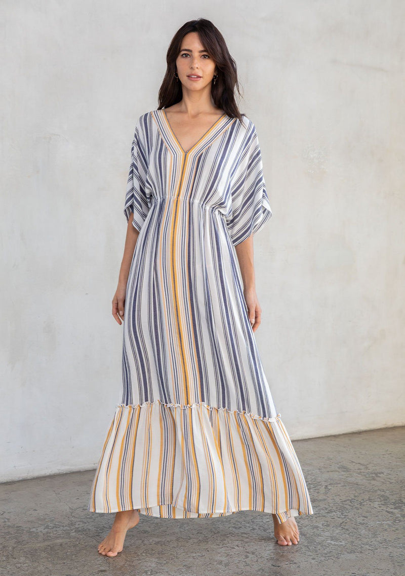[Color: Navy/Dijon] A model wearing a vacation worthy navy and yellow striped bohemian maxi dress. With short kimono sleeves, a tiered skirt, and an elastic waist. 