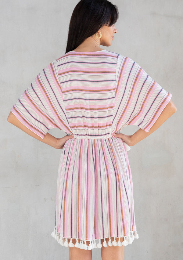 [Color: Natural/Pink] A model wearing a pink yarn dye stripe resort mini dress with tassel trim and crochet detail. 