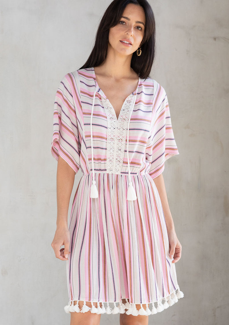 [Color: Natural/Pink] A model wearing a pink yarn dye stripe resort mini dress with tassel trim and crochet detail. 