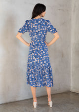 [Color: Navy/Cream] A model wearing a vintage inspired mid length wrap dress in a navy blue floral print. With short puff sleeves, a ruffled asymmetric hemline, and side tie closure.