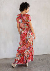 [Color: Ivory/Red] A model wearing an ultra bohemian flowy maxi dress in a red and pink floral patchwork print. With short puff sleeves and a rope waist belt. 