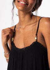 [Color: Black] A model wearing a flowy black bohemian summer maxi dress with strappy back and wooden bead details. 