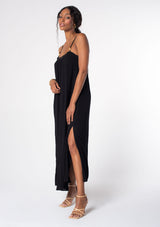 [Color: Black] A model wearing a flowy black bohemian summer maxi dress with strappy back and wooden bead details. 