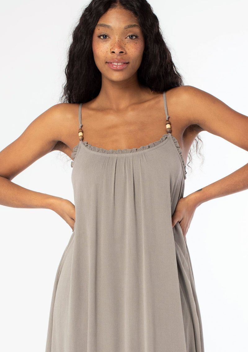 [Color: Cement] A close up front facing image of a black model wearing a flowy grey bohemian summer maxi dress with strappy back and wooden bead details.