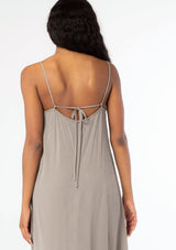 [Color: Cement] A close up back facing image of a black model wearing a flowy grey bohemian summer maxi dress with strappy back and wooden bead details.