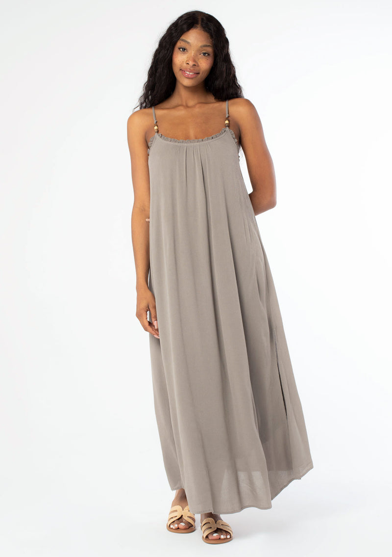 [Color: Cement] A front facing image of a black model wearing a flowy grey bohemian summer maxi dress with strappy back and wooden bead details.