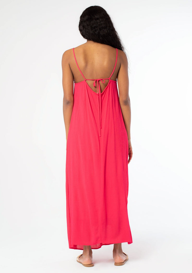 [Color: Hot Pink] A back facing image of a black model wearing a flowy bright pink bohemian summer maxi dress with strappy back and wooden bead details.