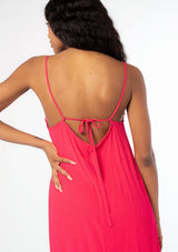 [Color: Hot Pink] A close up back facing image of a black model wearing a flowy bright pink bohemian summer maxi dress with strappy back and wooden bead details.