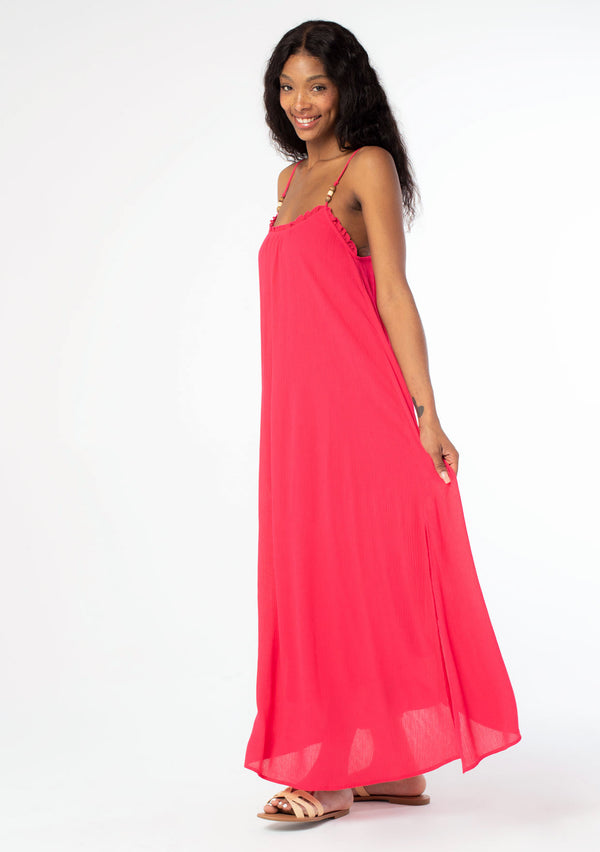 [Color: Hot Pink] A side facing image of a black model wearing a flowy bright pink bohemian summer maxi dress with strappy back and wooden bead details.