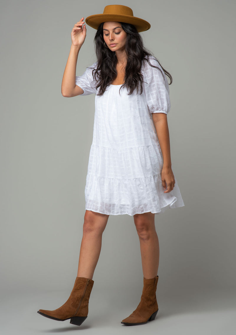 [Color: White] A model wearing a bohemian white cotton mini dress with short puff sleeves and a relaxed flowy fit.