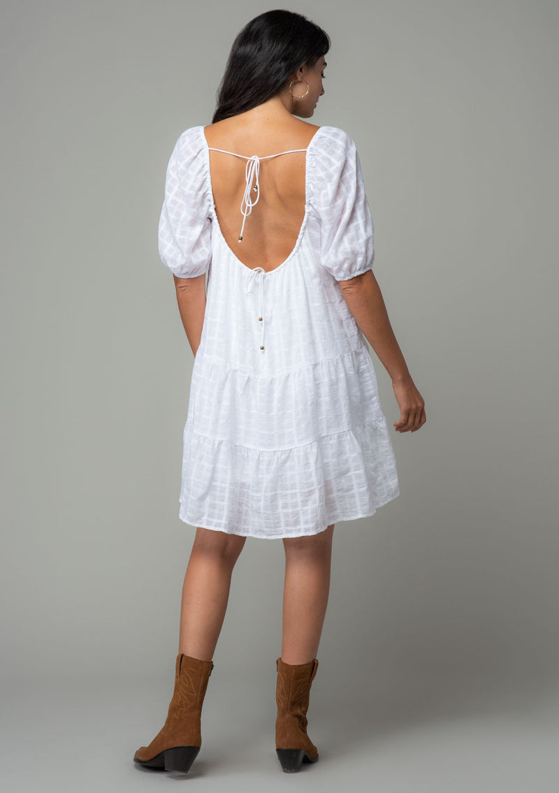 [Color: White] A model wearing a bohemian white cotton mini dress with short puff sleeves and a relaxed flowy fit.