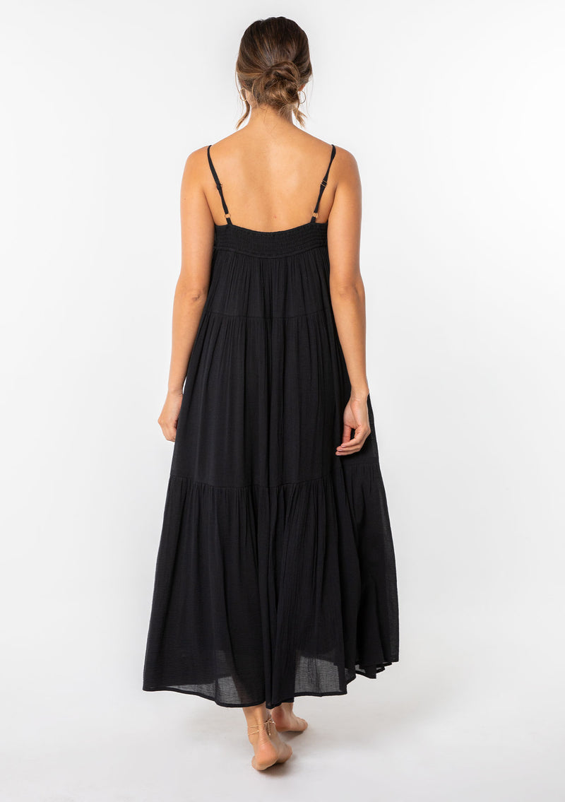 [Color: Black] A woman wearing a black flowy bohemian maxi dress with crochet trim, gold toned hardware, and adjustable spaghetti straps. 