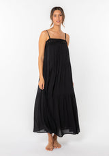 [Color: Black] A woman wearing a black flowy bohemian maxi dress with crochet trim, gold toned hardware, and adjustable spaghetti straps. 