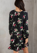 [Color: Black/Red] A model wearing a classic black bohemian mini dress in a pink floral print. With a loose, relaxed silhouette, long sleeves, and a split v neckline with tassel ties.