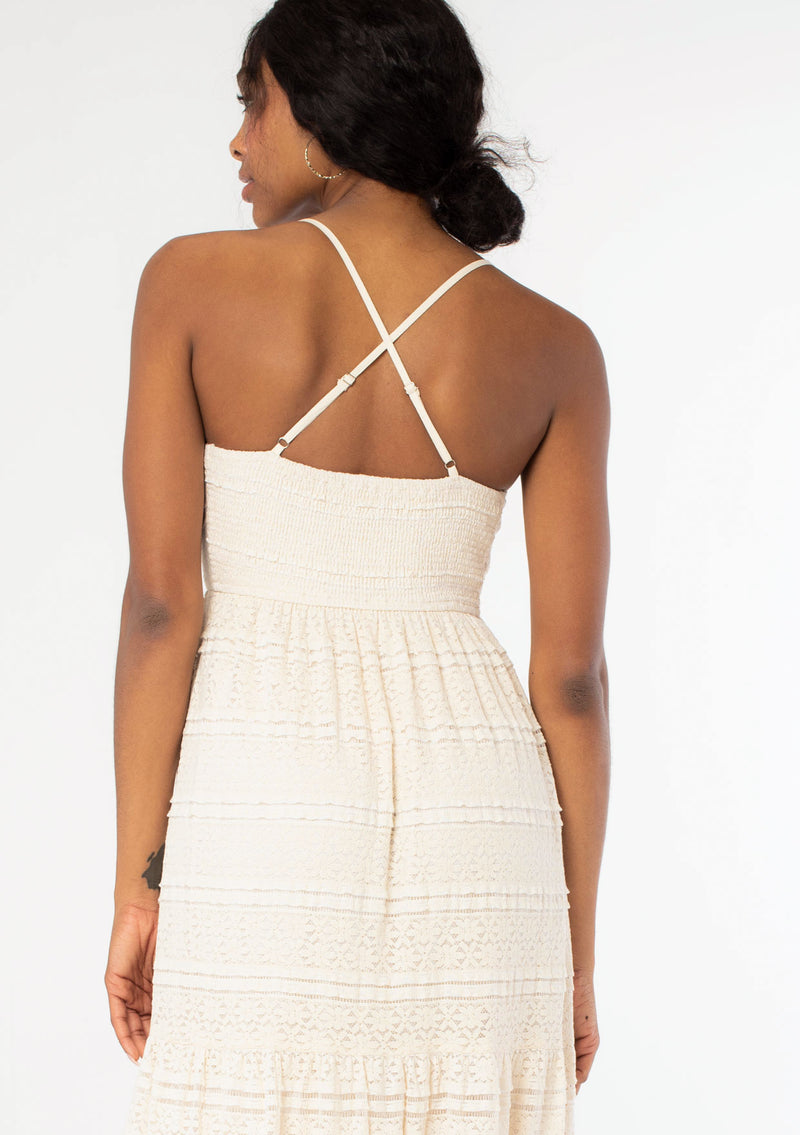 [Color: Natural] A close up back facing image of a black model wearing a bohemian off white lace maxi dress with spaghetti straps, a flowy skirt, and a v neckline.