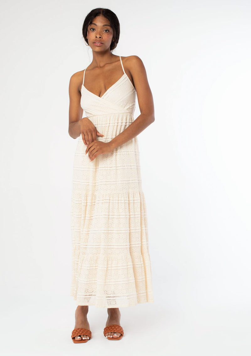 [Color: Natural] A front facing image of a black model wearing a bohemian off white lace maxi dress with spaghetti straps, a flowy skirt, and a v neckline.