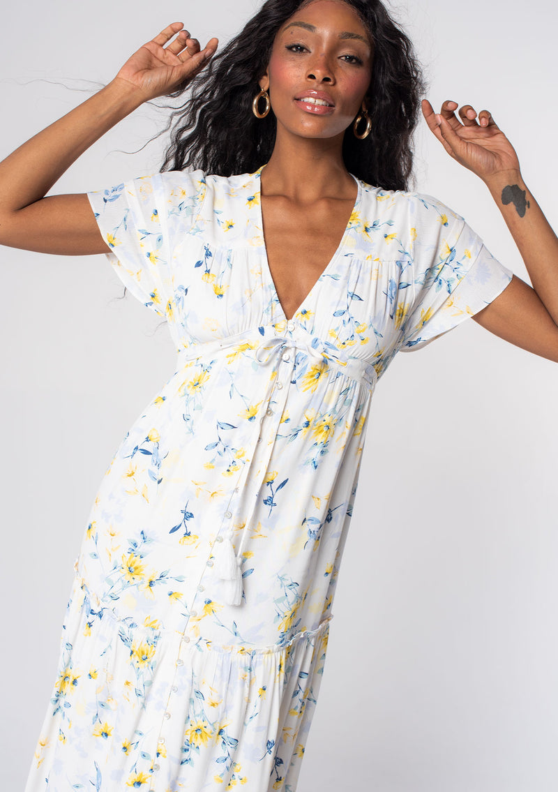 [Color: Cream/Yellow] A model wearing a white, yellow, and blue floral print bohemian maxi dress with short flutter sleeves and a flowy skirt. 