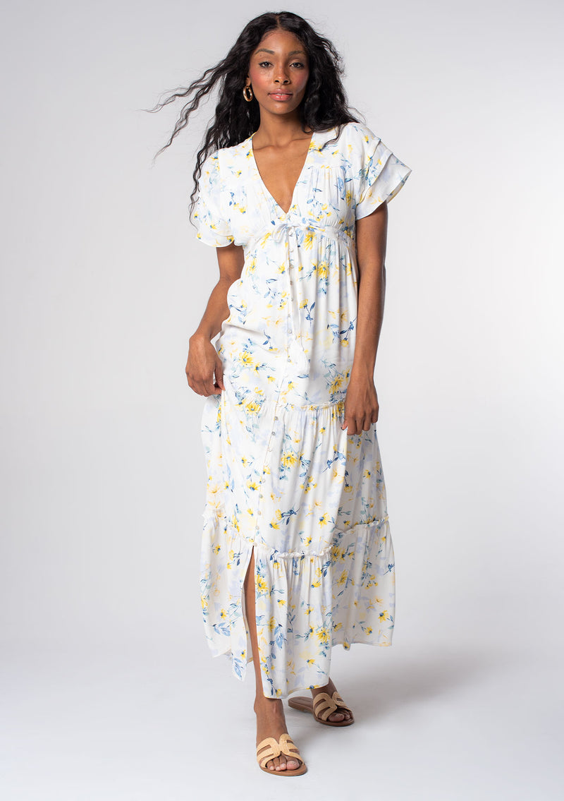 [Color: Cream/Yellow] A model wearing a white, yellow, and blue floral print bohemian maxi dress with short flutter sleeves and a flowy skirt. 