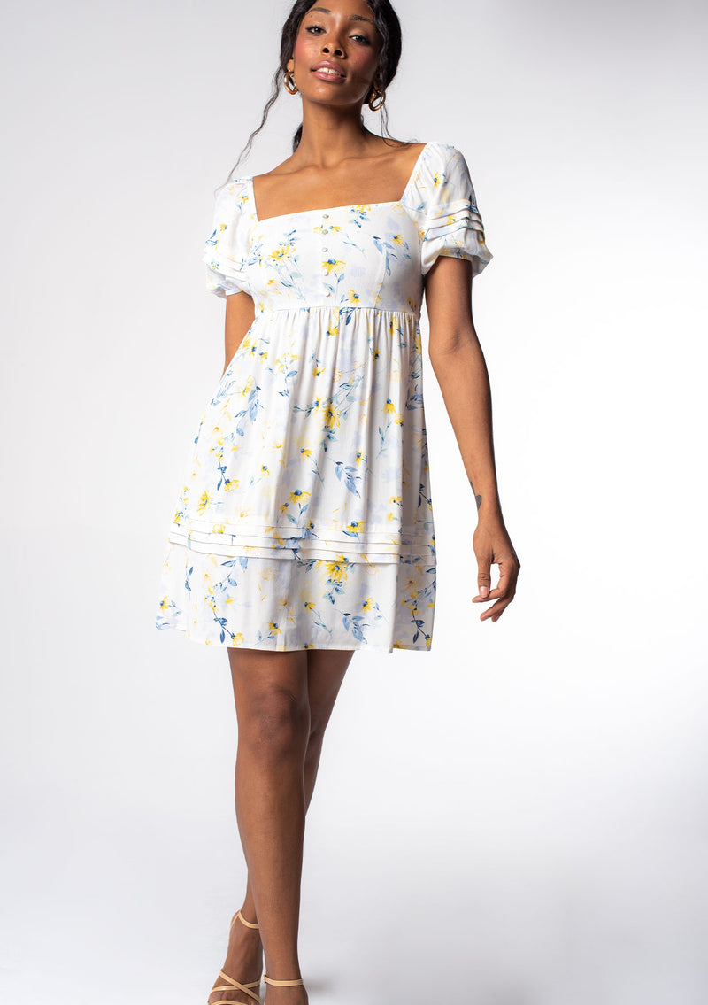 [Color: Cream/Yellow] A model wearing a white, yellow, and blue floral print puff sleeve mini dress. 