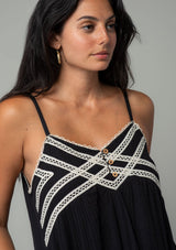 [Color: Black/Natural] A close up front facing image of a brunette model wearing a black cotton gauze sleeveless maxi dress with a natural crochet trim top and hemline. With adjustable spaghetti straps and a flowy fit. 