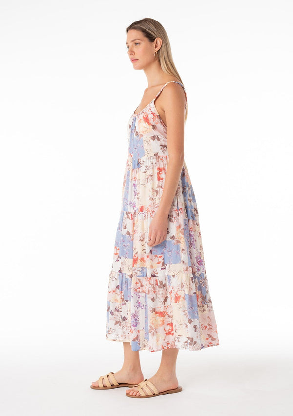 [Color: Natural/Rust] An angled side facing image of a blonde model wearing an ultra flowy cotton bohemian spring maxi dress in a pink and blue floral print. With elastic tank top straps, a scooped neckline, a low back, a tiered silhouette, and side pockets. 