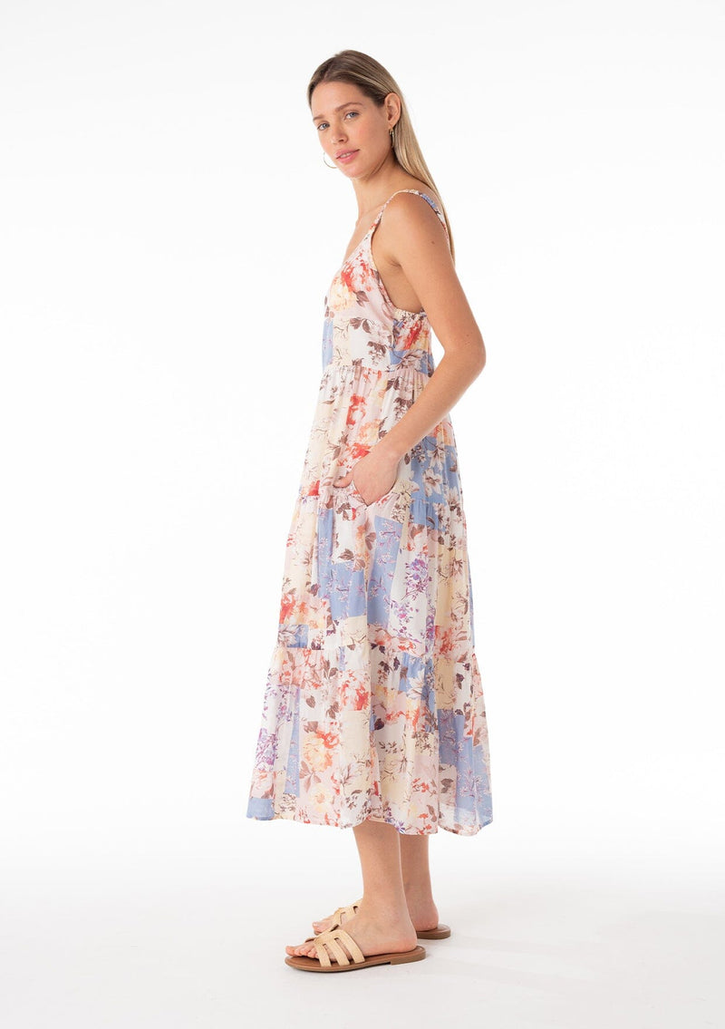[Color: Natural/Rust] A side facing image of a blonde model wearing an ultra flowy cotton bohemian spring maxi dress in a pink and blue floral print. With elastic tank top straps, a scooped neckline, a low back, a tiered silhouette, and side pockets. 