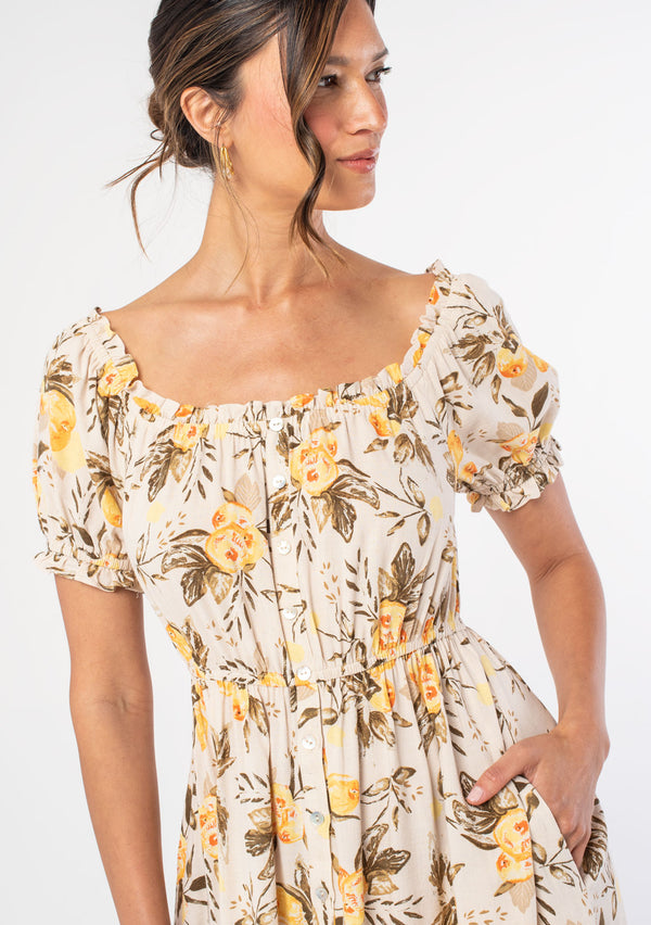 [Color: Natural/Yellow] A model wearing a natural and yellow floral fruit print mini dress with short puff sleeves and an optional off shoulder ruffled neckline. 