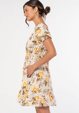 [Color: Natural/Yellow] A model wearing a natural and yellow floral fruit print mini dress with short puff sleeves and an optional off shoulder ruffled neckline. 