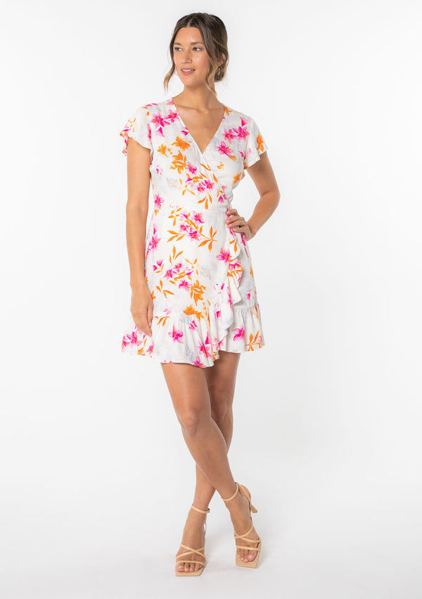 [Color: Ivory/Fuchsia] A model wearing a white and pink floral print mini wrap dress with short flutter sleeves and ruffled hemline. 