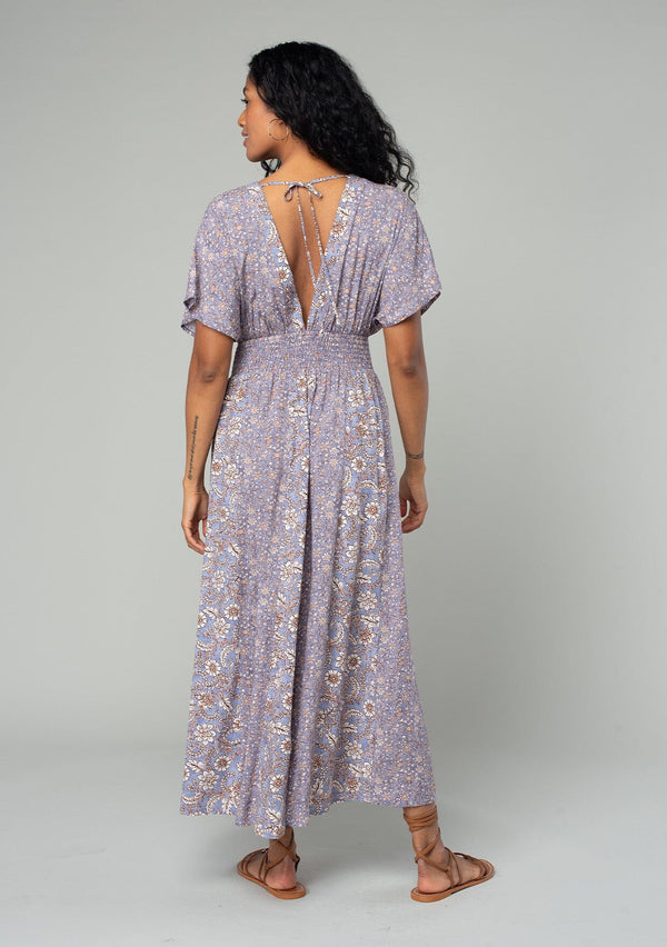 [Color: Grey/Natural] A back facing image of a brunette model wearing a flowy bohemian resort maxi dress in a grey and purple mixed floral print. With short kimono sleeves, an open back with tie closure, a smocked elastic waist, and a side slit. 