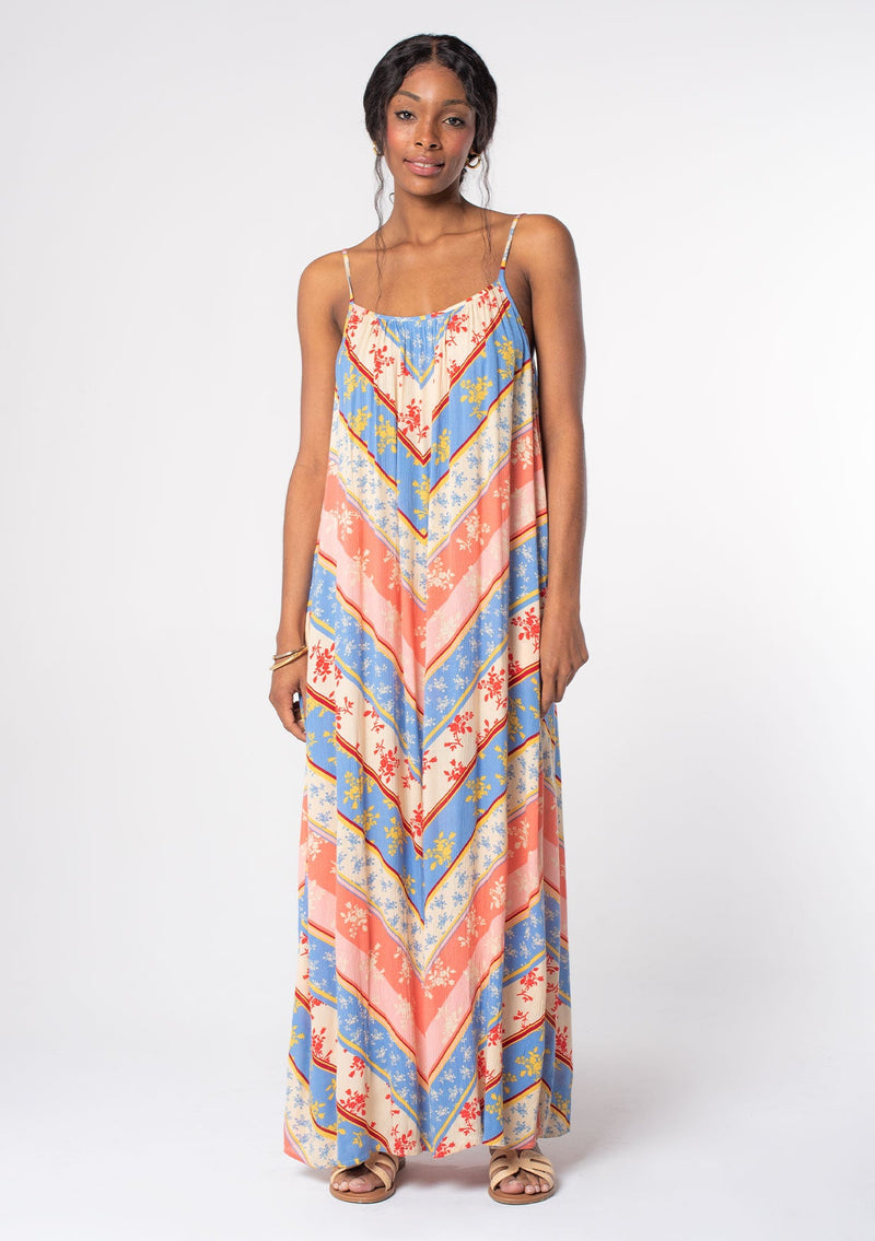 [Color: Indigo/Red] A model wearing a flowy relaxed bohemian beach maxi dress in a blue and red floral chevron stripe print. With adjustable spaghetti straps and a scooped neckline. 