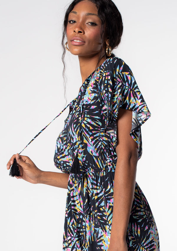 [Color: Black/Blue] A model wearing a bohemian black summer mini dress with multi color palm print and short flutter sleeves. 