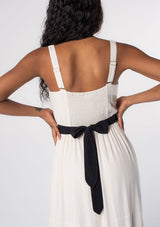[Color: Vanilla/Black] A model wearing an elegant, timeless white and black maxi dress in a linen blend, with tank top straps, a v neckline, and a contrast waist belt that ties in the back. 