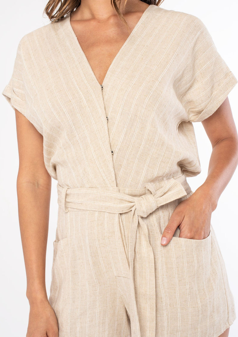 [Color: Natural] A woman wearing a natural linen stripe short romper with a tie waist and side pockets. 