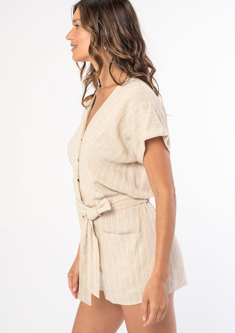 [Color: Natural] A woman wearing a natural linen stripe short romper with a tie waist and side pockets. 