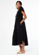 [Color: Black] A side facing image of a black woman wearing a black cotton mid length dress with a smocked top, button front skirt, and a loose, relaxed fit.