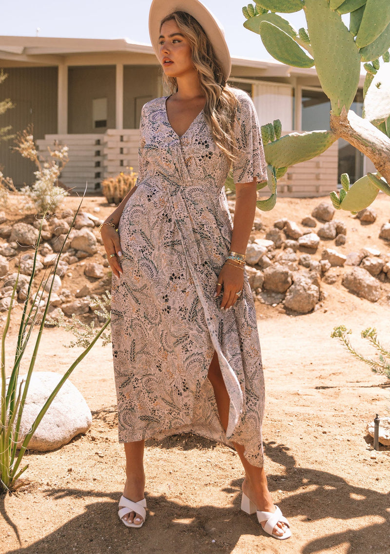 [Color: Natural/Olive] A front facing image of a blonde model wearing a natural and olive green floral print maxi dress, with short sleeves, a faux wrap front, and a front slit.