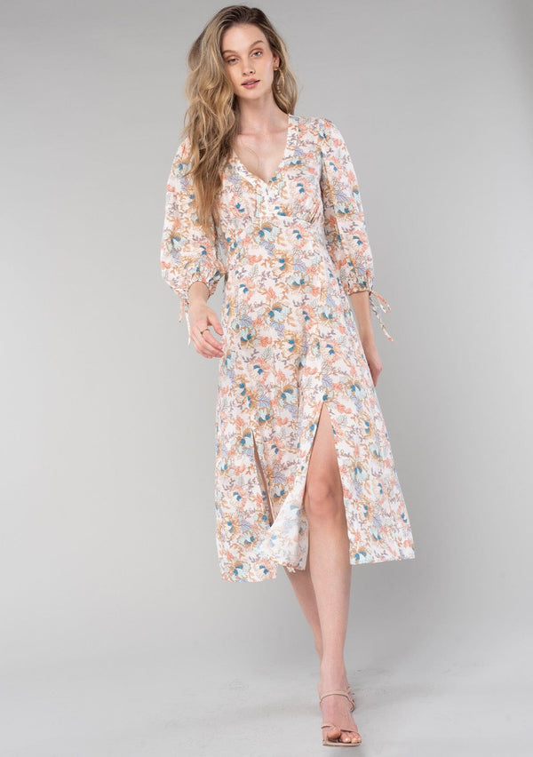 [Color: Natural/Coral] A full body front facing image of a blonde model wearing a bohemian spring mid length dress in a natural and coral floral print. With half length sleeves, tie cuffs, side slits, and a v neckline. 