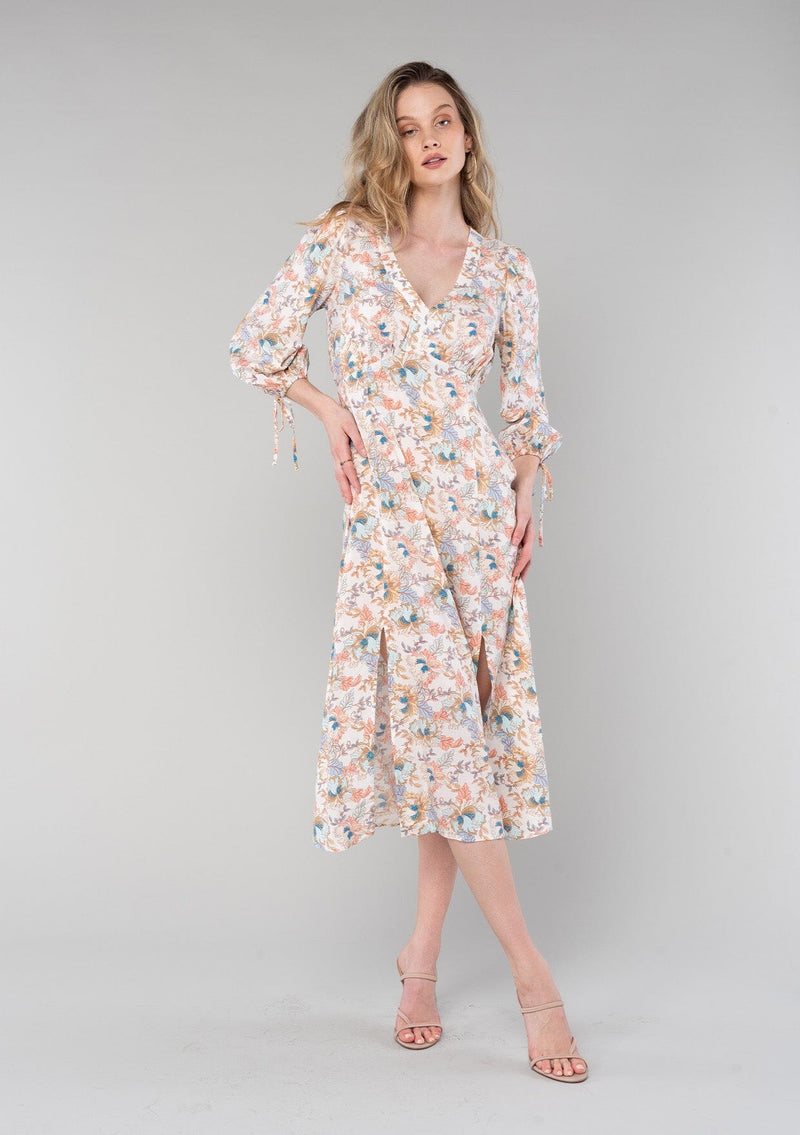 [Color: Natural/Coral] A front facing image of a blonde model wearing a bohemian spring mid length dress in a natural and coral floral print. With half length sleeves, tie cuffs, side slits, and a v neckline. 