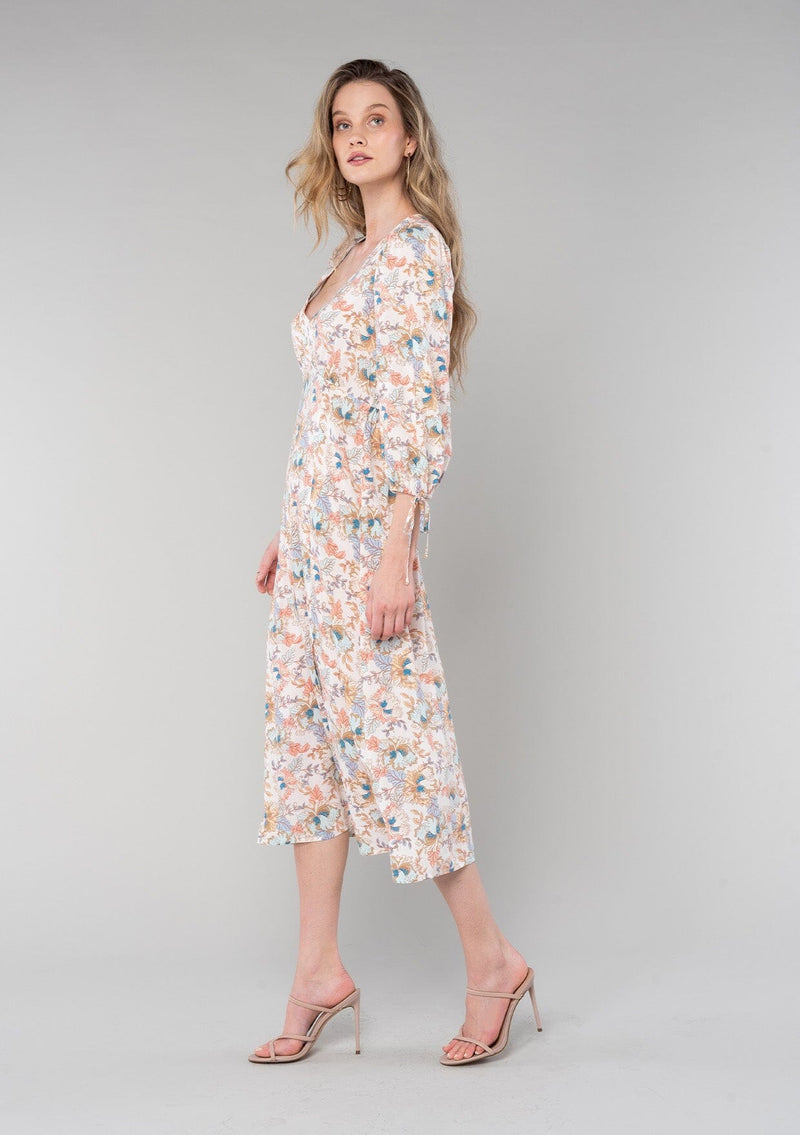 [Color: Natural/Coral] A side facing image of a blonde model wearing a bohemian spring mid length dress in a natural and coral floral print. With half length sleeves, tie cuffs, side slits, and a v neckline. 