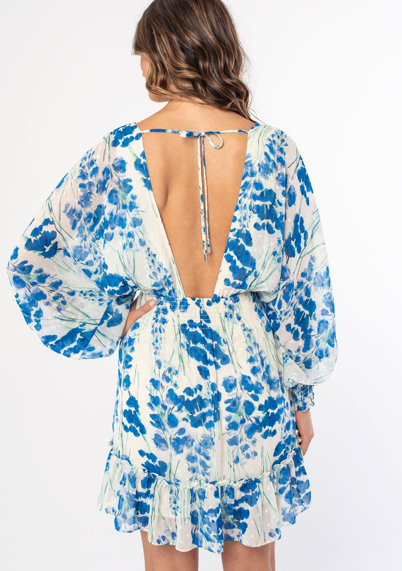 [Color: Cream/Blue] A model wearing a sheer clip dot chiffon mini dress in a cream and blue watercolor floral print. With voluminous long sleeves and an open back.