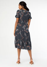 [Color: Charcoal/Dusty Blue] A full body back facing image of a black model wearing a charcoal dark grey mid length dress with blue paisley dot print throughout. A bohemian midi dress with short puff sleeves, a flowy tiered skirt, and a self tie waist belt. 