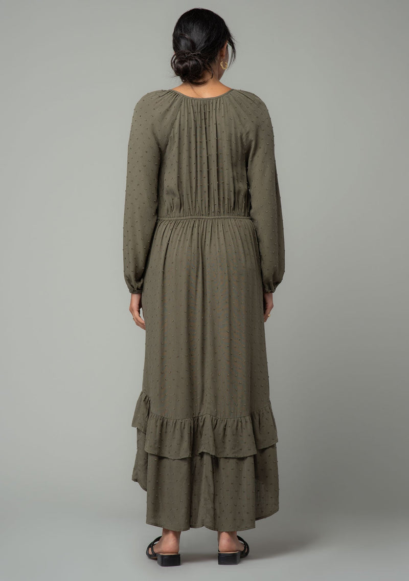 [Color: Olive] A back facing image of a brunette model wearing an olive green high low maxi dress with a ruffled hemline, voluminous long sleeves, and a drawstring tassel tie waist. 