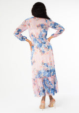 [Color: Lavender/Denim Blue] A back facing image of a black model wearing a lavender purple and blue floral print bohemian chiffon maxi dress. With long sleeves, a self covered button front, and an elastic waist. 