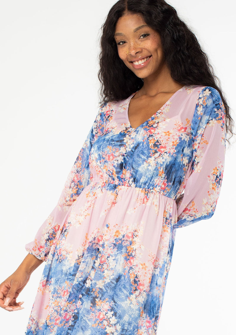 [Color: Lavender/Denim Blue] A close up front facing image of a black model wearing a lavender purple and blue floral print bohemian chiffon maxi dress. With long sleeves, a self covered button front, and an elastic waist. 