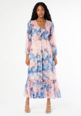 [Color: Lavender/Denim Blue] A front facing image of a black model wearing a lavender purple and blue floral print bohemian chiffon maxi dress. With long sleeves, a self covered button front, and an elastic waist. 
