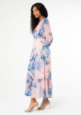 [Color: Lavender/Denim Blue] A side facing image of a black model wearing a lavender purple and blue floral print bohemian chiffon maxi dress. With long sleeves, a self covered button front, and an elastic waist. 