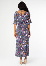 [Color: Navy/Berry] A back facing image of a black model wearing a navy blue and berry purple vintage floral print maxi dress with half length sleeves, a smocked elastic waist, and an open back with tassel ties. 