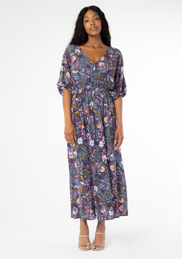 [Color: Navy/Berry] A full body front facing image of a black model wearing a navy blue and berry purple vintage floral print maxi dress with half length sleeves, a smocked elastic waist, and an open back with tassel ties. 